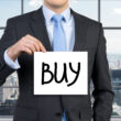Mężczyzna trzymający kartkę z napisem "buy" jako symbol rekomendacji w tradingu